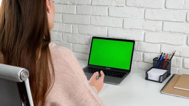 Lehrerin zu Hause sitzt mit Stift in der Hand am Tisch und spricht mit grünem Bildschirm-Laptop - Foto, Bild