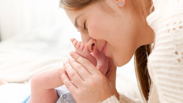 A boldog szerető anya portréja, amint csókol és kisbaba lábakat tart a bölcsőben. A családi boldogság fogalma és a kisgyermekes szerető szülők - Fotó, kép