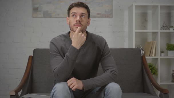 ustaraný muž sedí a přemýšlí v obývacím pokoji - Záběry, video