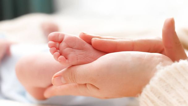 Tiny baby feet in female hands. Young mother gently touching and stroking her newborn baby legs. Concept of family happiness and loving parents with little children. - Photo, Image