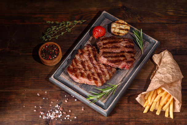 Свежий сочный вкусный говяжий стейк на темном фоне. Мясное блюдо со специями и травами - Фото, изображение