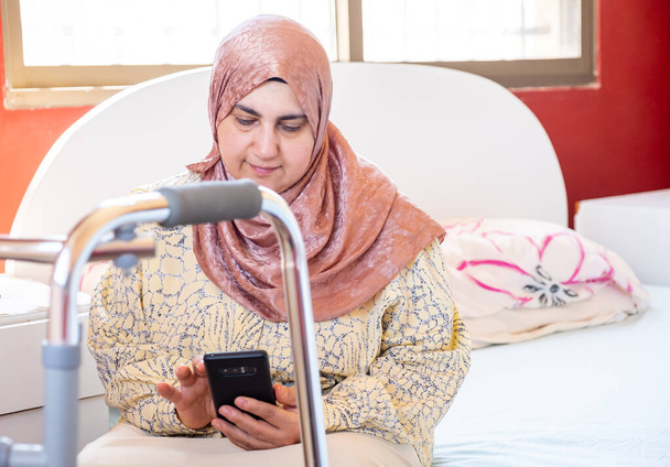 Muslimische Frau mit Behinderung tippt auf ihrem Handy - Foto, Bild