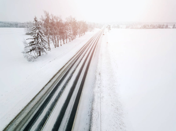 Vue de drone d'une route pavée avec des voitures avec leurs phares allumés au loin par une journée nuageuse d'hiver. Beau paysage d'hiver - Photo, image