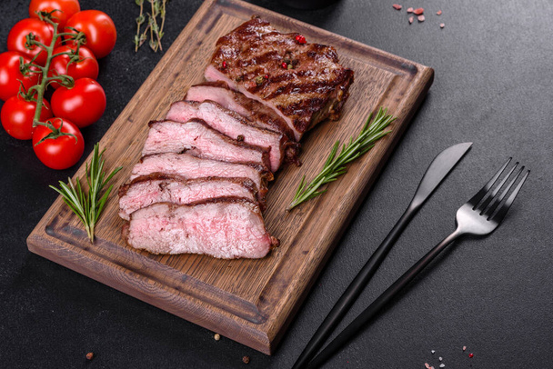 Čerstvé šťavnaté chutné hovězí steak na tmavém pozadí. Masová mísa s kořením a bylinkami - Fotografie, Obrázek