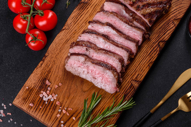 Frisch saftiges, köstliches Rindersteak auf dunklem Hintergrund. Fleischgericht mit Gewürzen und Kräutern - Foto, Bild