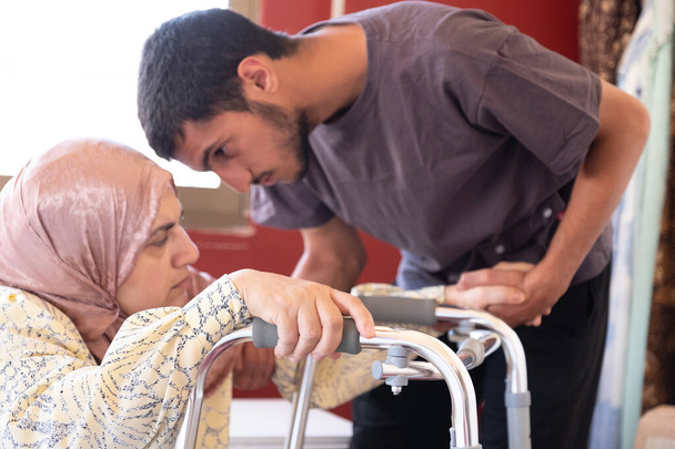 Muslimische Frau mit Behinderung versucht, mit der Hilfe ihres Sohnes durchzuhalten - Foto, Bild