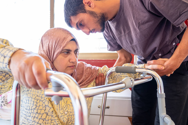 mujer musulmana con discapacidad está tratando de estar de pie con la ayuda de su hijo - Foto, imagen