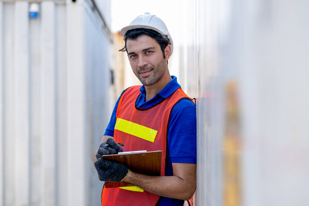 Cargo container worker or foreman hold clipboard and look to camera and stand in workplace area. Industrial and factory support system of logistics import export concept. - Photo, Image