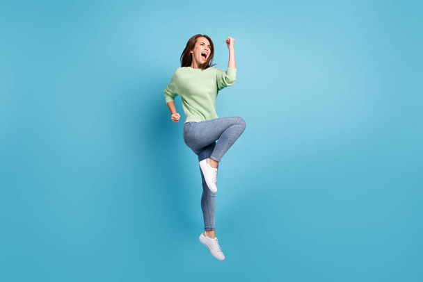 Full length body size photo of young jumping happily girl wearing casual jumper jeans screaming loudly gesturing like a winner isolated on bright blue color background - Foto, immagini