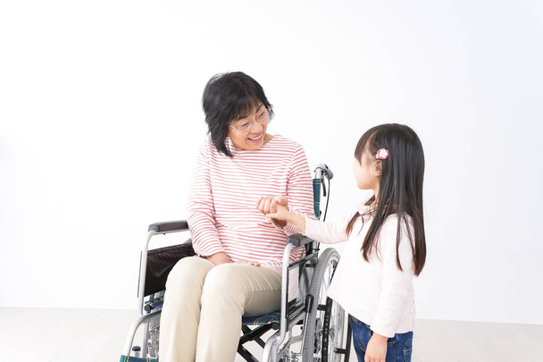 Азійська дівчинка і старша жінка в інвалідному візку. - Фото, зображення