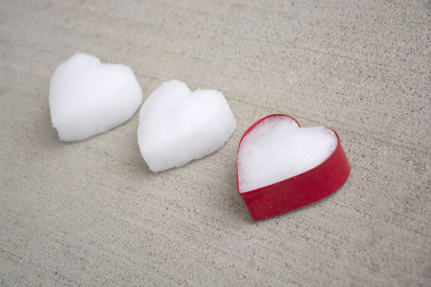  White hearts made of snow with one red colored cookie cutter laying on grey concrete background surface, vintage look. Selective focus. Flat lay, Top view. - Photo, Image