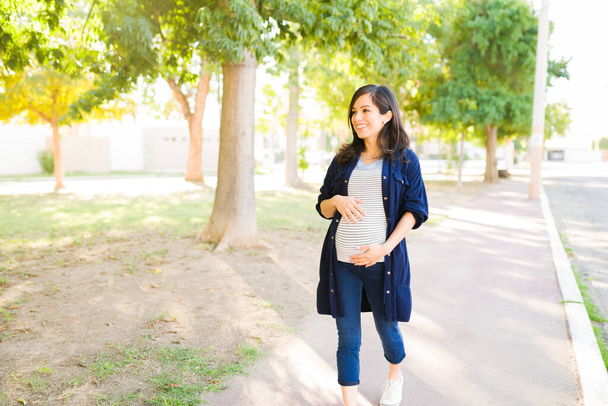 Щаслива вагітна жінка гуляє в парку. Красива активна жінка посміхається і насолоджується прогулянкою на відкритому повітрі
  - Фото, зображення