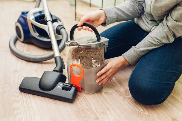 Женщина открывает пылезащитный фильтр из пылесоса дома на полу. Контейнер с грязью и кошачьими волосами. Домашняя работа - Фото, изображение