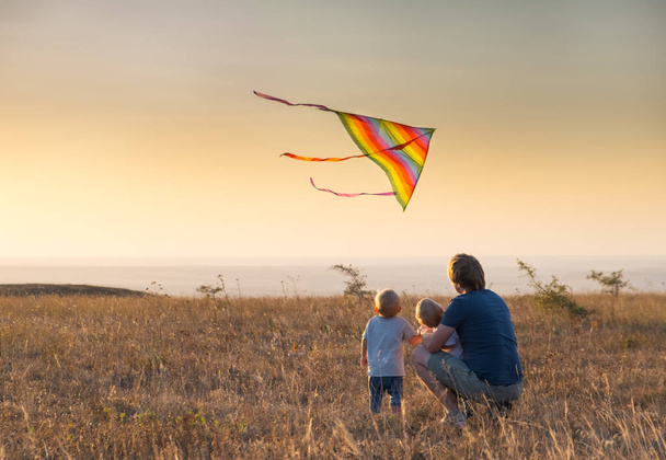 Ο μπαμπάς και τα παιδιά πετάνε χαρταετό το ηλιοβασίλεμα. - Φωτογραφία, εικόνα