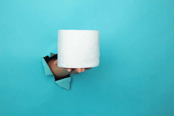 Female hand holds toilet paper through torn blue paper background - Photo, Image