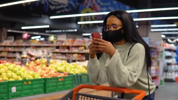 Girl in a mask talking on the phone in the supermarket - Filmati, video