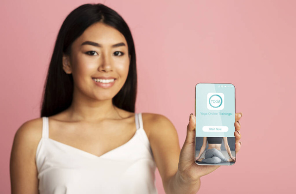 Азіатська жінка показує телефон з онлайн-додатком йоги, рожевий фон
 - Фото, зображення