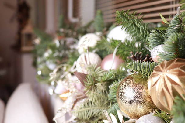 ein künstlicher grüner Zweig einer Tanne mit Girlanden, die mit Weihnachtsspielzeug und Kugeln aus Gold und weißer Farbe verziert sind - Foto, Bild