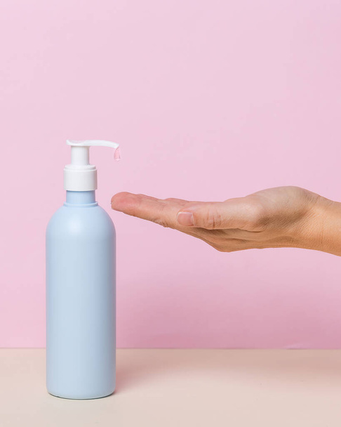 Female hand using alcohol gel sanitizer bottle dispenser, against coronavirus disease (Covid-19) . Antiseptic, Hygiene and Health concept. Minimalist style on pink background - Photo, Image