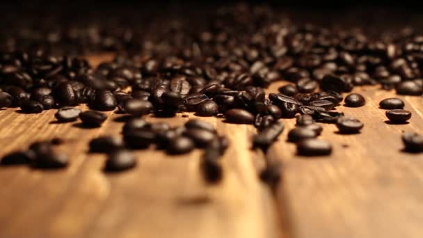 Granos de café tostados que caen sobre una mesa de madera cubierta con granos de café - Imágenes, Vídeo
