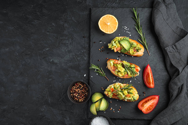 Toast with avocado, tomato and rosemary on a black concrete table. - Photo, image
