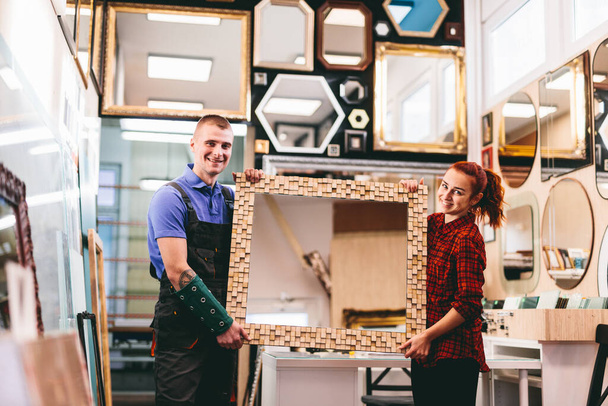 Владельцы малого бизнеса демонстрируют зеркало с деревянной рамой ручной работы в местном магазине. - Фото, изображение