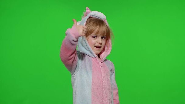 Petite fille enfant souriant, montrant les pouces vers le haut geste, signe d'accord en pyjama licorne sur la touche chroma - Photo, image
