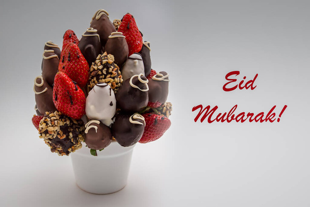 Eid Mubarak Grußkarte mit rotem Schriftzug; Ein Bund essbarer Blumen, Anordnung von Erdbeeren in Schokolade getaucht isoliert auf weißem Hintergrund - Foto, Bild
