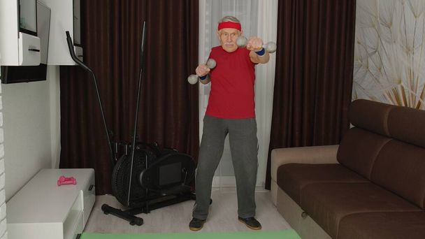 Старший чоловік робить життєво важливі вправи для важкої атлетики з гантелями вдома під час коронавірусу
 - Фото, зображення