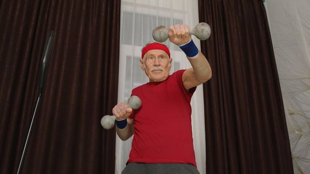 Старший літній чоловік у спортивному одязі робить вагові підйомні гантелі тренування кардіо вправи вдома
 - Фото, зображення