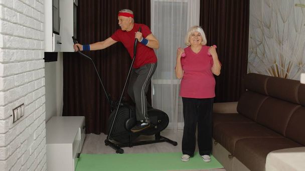 Senior elderly couple using orbitrek, doing workout weight lifting sport dumbbells exercises at home - Photo, Image