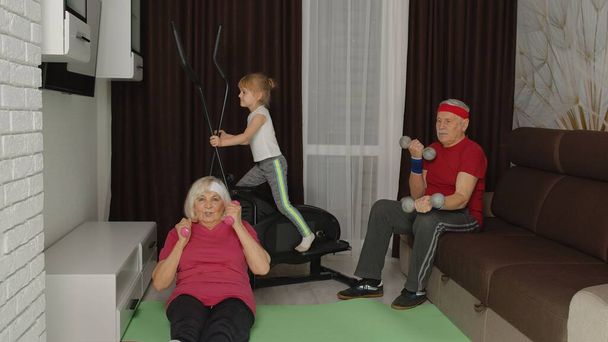 Старшие дедушка и бабушка используют орбитальный аппарат, выполняя упражнения по поднятию гантели - Фото, изображение