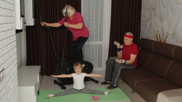 Senior couple with granddaughter using orbitrek, doing weight lifting dumbbells exercises at home - Photo, Image