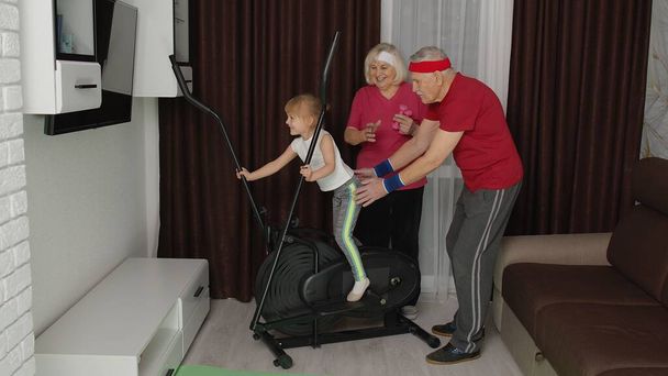 Niña usando orbitrek en casa haciendo ejercicios de entrenamiento deportivo ejercicios de cardio con entrenadores abuelos - Foto, Imagen