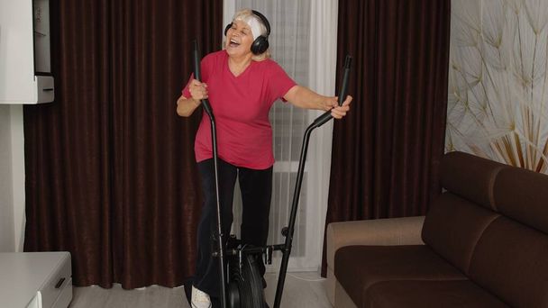 Aktiivinen terve vanhempi kypsä vanha nainen urheiluvaatteet käyttäen orbitrek, koulutus sydän harjoitus kotona - Valokuva, kuva