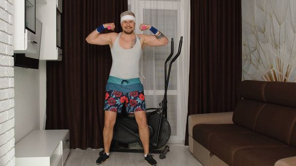 Funny culturista deportista sofá chico mostrando bíceps, ejercicios de boxeo fitness deporte con pesas - Foto, Imagen