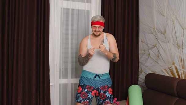 Deportista retro chico en ropa divertida bailando en casa, hombre haciendo deporte ejercicios de ejercicio cardiovascular - Foto, Imagen