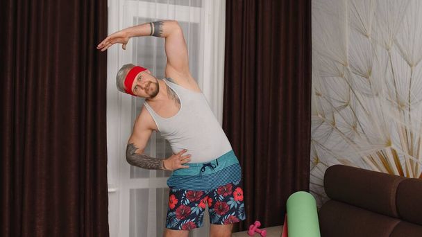 Смешной спортсмен спортсмен с бородой делает упражнения на растяжку, занимаясь спортом дома - Фото, изображение