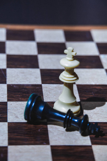 selektivní zaměření černého krále šachové figurky u nohou bílého krále s kopírovacím prostorem a nadřazenost koncept vítězství a triumf - Fotografie, Obrázek