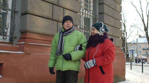 シニアカップル男性、冬の話で旧市街を歩く女性観光客、休暇をジェスチャー - 写真・画像