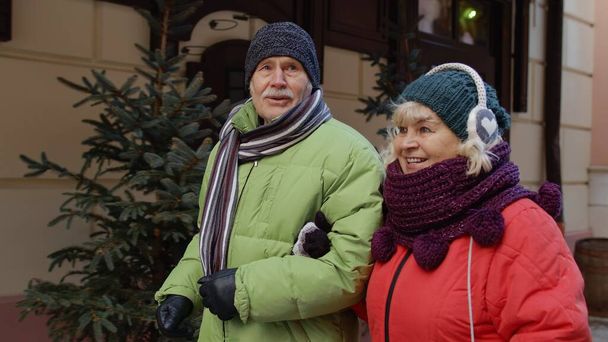 Feliz pareja de ancianos turistas hombre y mujer caminando, hablando, gesticulando en invierno nevado ciudad europea - Foto, imagen