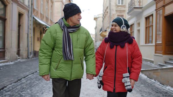 高齢者のカップル観光客の男性女性が一緒に時間を楽しんで、冬の街の通りに沿って歩く - 写真・画像
