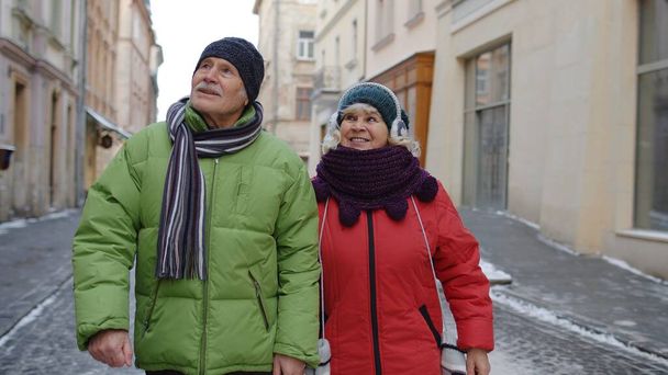 シニア老夫婦の観光客男性女性家族歩く、話す、冬の雪の街の通りでジェスチャー - 写真・画像