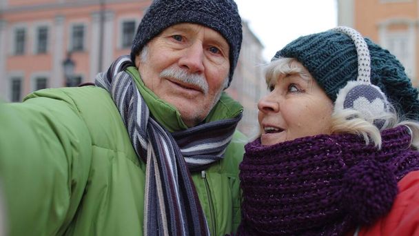 Un par de turistas mayores tomando selfie en invierno centro de la ciudad sonriendo, mirando a la cámara, blog, vlog - Foto, imagen