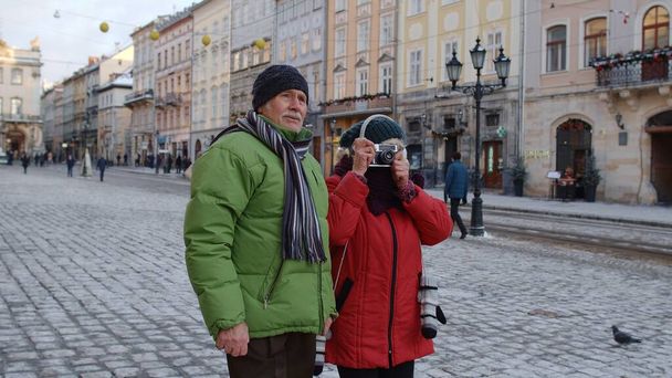 祖父は冬の雪の町のレトロカメラで祖母と一緒に写真を撮る｜Livv Ukraine - 写真・画像