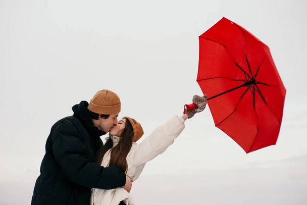 Young hipster couple walking with two red umbrellas in cold weather, love story outdoors - Photo, Image