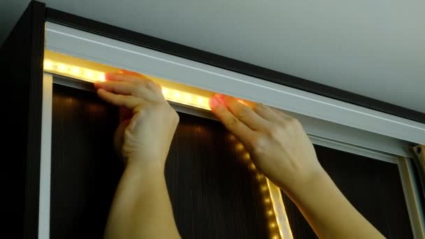 Мастер приклеивает светодиодную ленту к металлическому профилю шкафа - Кадры, видео