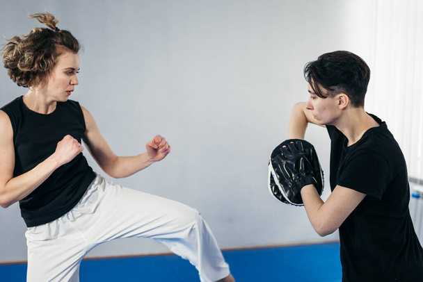 Close-up van blootsvoets vrouwenbeen dat traint te schoppen met taekwondo coach die bokspoot vasthoudt. Geconcentreerde actieve vrouwelijke schoppen boksen schild met persoonlijke coach in de sportschool. Vechters trainen samen. - Foto, afbeelding