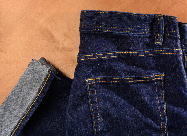 木製の背景に青いジーンズの断片。フラットレイアウト男性スタイル。ショッピングコンセプト。ファッショナブルな衣装。コピースペース. - 写真・画像