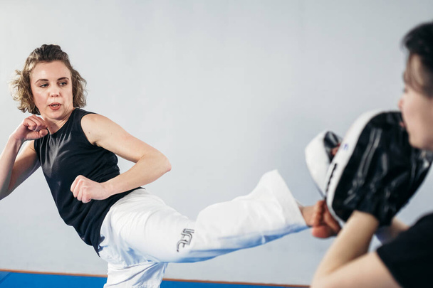 Προσωπική εκπαίδευση πολεμικής τέχνης του taekwondo. Γυναίκα εκπαιδεύτρια κρατώντας taekwondo kick pad, αθλητής εκπαιδευτές κλωτσιές. Γυναίκα κλοτσιές ασπίδα απεργία, προπόνηση πυγμαχίας με πούλμαν. Εκπαίδευση μαχητών μαζί. - Φωτογραφία, εικόνα